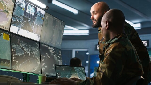 Army colleagues looking at screens in command center housing operational missile defense system designed to intercept ballistic rockets. Experts using tracking gear and radar systems, camera A