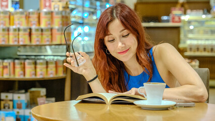 A beautiful young woman with red hair and glasses, wearing a blue t-shirt, is sitting in a lovely...
