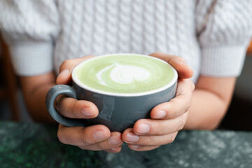 Warm hands cradle a matcha latte with heart foam art, creating a cozy and inviting atmosphere.