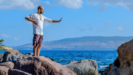 A middle-aged charismatic man, wearing a white shirt, is relaxing and enjoying the sun by doing...
