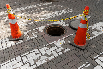 An open manhole cover on the street - Traffic cones located at the entrance to the sewer.