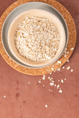 Oats in a bowl on a cork mat, with some scattered around on a brown surface, highlighting natural texture and simplicity