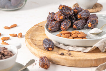 Medjool dates and almonds on a wooden board with a bowl of chocolate chunks and a bowl of almonds in the background, creating a rustic and healthy snack setup