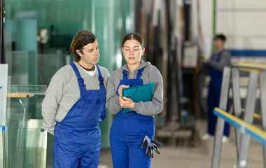 Adult guy and young woman with folder glass factory workers discuss work process