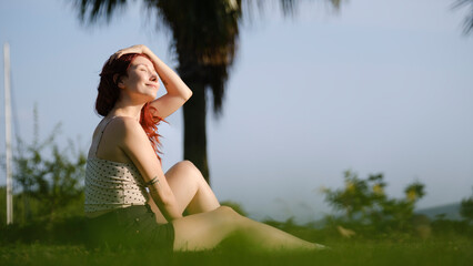 Moments when a beautiful young red-haired woman spends time and has fun in a grassy area of the...