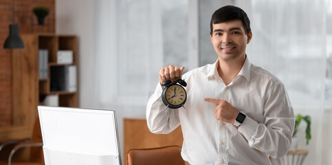 Young businessman pointing at alarm clock in office