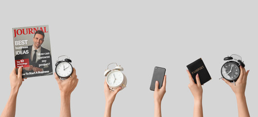 Hands holding alarm clocks, mobile phone, passport and magazine on grey background