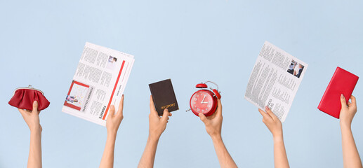 Hands holding alarm clock, newspapers and wallets on blue background