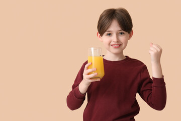 Happy little boy with glass of orange juice on beige background