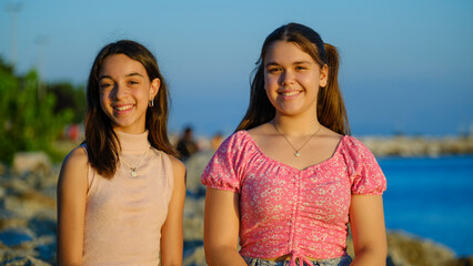 Two teenage girls friends, one slightly overweight and the other with dark skin, sitting on the...