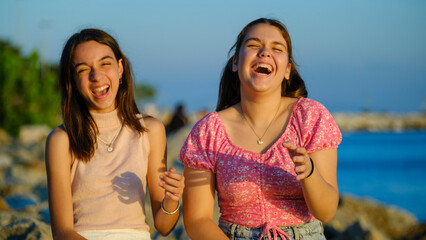 Two teenage girls friends, one slightly overweight and the other with dark skin, sitting on the...