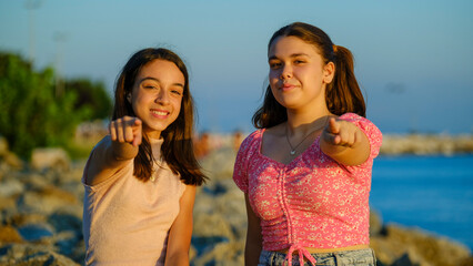 Two teenage girls friends, one chubby and the other with dark skin, sitting on the rocks by the...