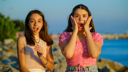 Two teenage girls friends, one chubby and the other with dark skin, sitting on the rocks by the...