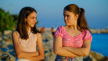 Two teenage girls friends, one chubby and the other with dark skin, sitting on the rocks by the...