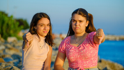 Two teenage girls friends, one chubby and the other with dark skin, sitting on the rocks by the...