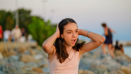 A dark-skinned teenage girl sitting on the rocks by the seaside on a sunny summer day, showing a...