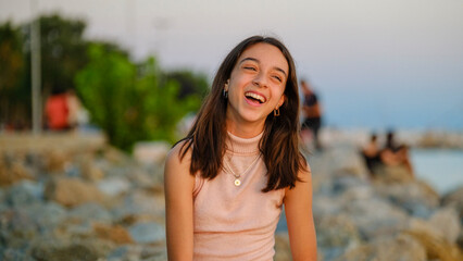 A dark-skinned teenage girl sitting on the rocks by the seaside on a sunny summer day, looking at...