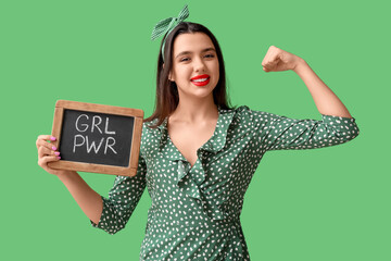 Beautiful young happy pin-up woman holding blackboard with text GIRL POWER and showing muscles on...