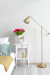 Vase with tulips and Easter wreath on table in light bedroom