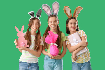 Cute little girls with Easter bunny ears, gifts and decor on green background