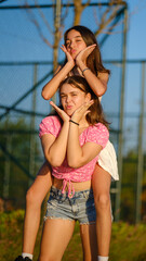 A somewhat chubby teenage girl carrying her dark-skinned friend on her back in a park, playing and...