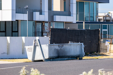 a large industrial waste bin or dumpster in front of a modern residential building or new suburban...