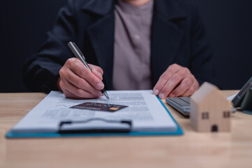 A woman is writing on a piece of paper with a pen. She is holding a credit card in her hand