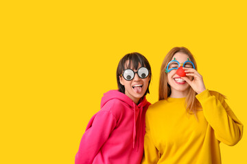 Beautiful young happy women in funny disguise on yellow background. April Fools Day celebration