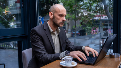 A middle-aged handsome businessman in a suit working with his laptop outside the office...