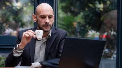 A middle-aged handsome businessman in a suit working with his laptop outside the office...