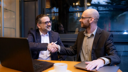 Two middle-aged businessmen, are having a meeting outside the office in a cafe environment, working...