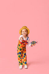 Cheerful little girl in clown costume and hat with paper fish on pink background