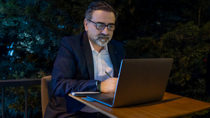 Mature handsome businessman in suit working with laptop outside office environment with full focus