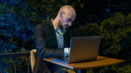 A middle-aged handsome businessman in a suit working with his laptop outside the office...