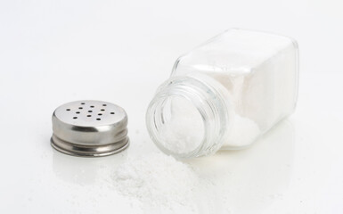 Salt shaker tipped over with granules scattered on a white surface in a kitchen setting