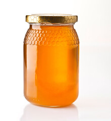 Freshly harvested honey in a clear jar with a golden lid on a white background