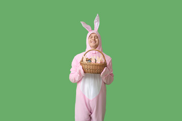 Happy young man in Easter bunny costume with basket on green background