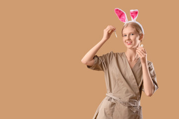 Young female massage therapist in bunny ears with bottle of essential oil on color background
