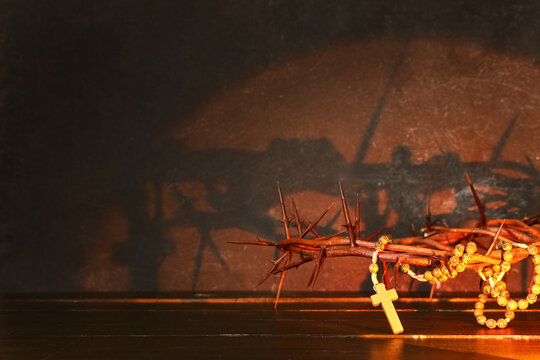 Crown of thorns and beads with cross on wooden table against black grunge background. Good Friday concept