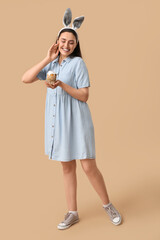 Beautiful young woman in bunny ears with sweet Easter cake on brown background