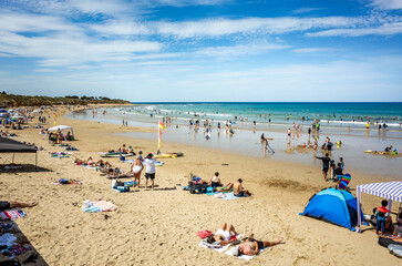 Summer scene at Torquay Surf Beach, Australia, with beachgoers sunbathing, swimming, and enjoying...