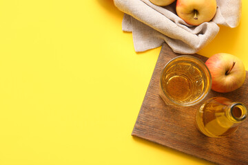Wooden tray, bottle and glass of fresh apple cider on yellow background