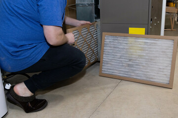 homeowner preforming general maintenance on home furnace, replacing the old dirty filter with a...