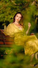 A beautiful young brown-haired woman models stylishly in a wooded area on a summer day, posing...