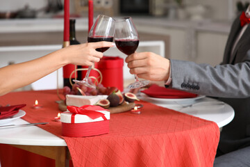 Loving young couple having romantic dinner with wine and gift box at home, closeup. Valentine's Day celebration