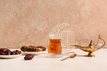 Aladdin lamp, glass cup of tea and dates on white table against beige background. Ramadan...