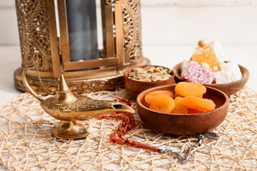 Aladdin lamp, prayer beads, Muslim lantern and traditional food on white table against wooden background. Ramadan celebration