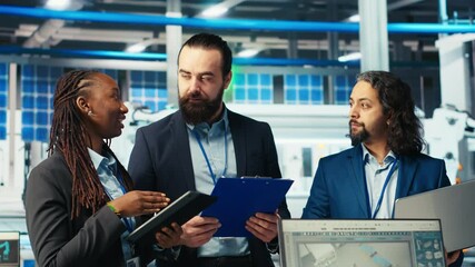 Portrait of cheerful experts in photovoltaics factory reviewing performance of robot arms placing solar panels on assembly lines. Team of upbeat business partners inspecting solar plant machinery