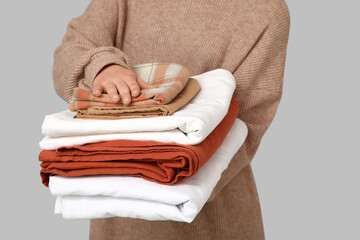 Young woman holding stack of clean bed sheets on light background, closeup