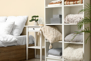Shelving unit with clean bed sheets, boxes and plaid in bedroom